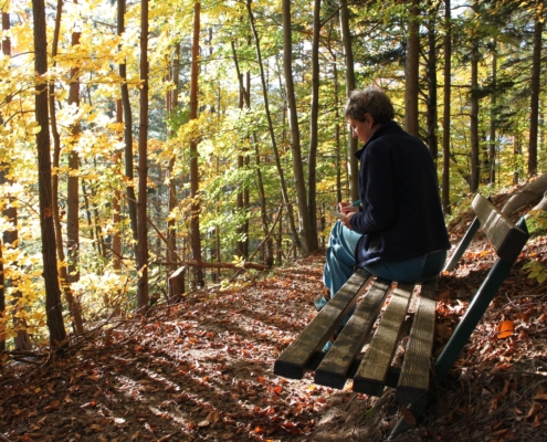 Frau sitzt auf Bank im Herbstwald und schreibt